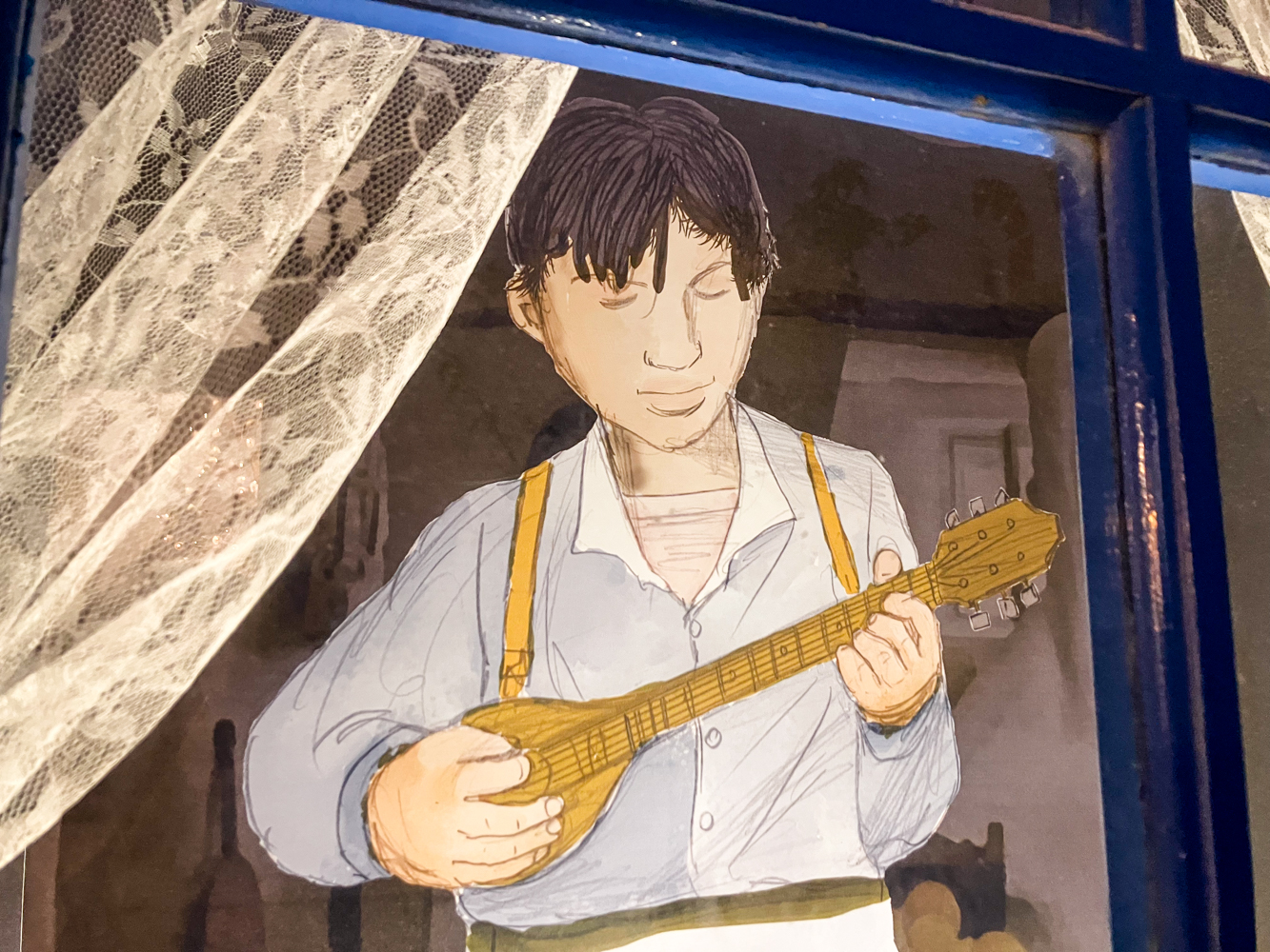 Fenêtre décorée avec un musicien qui joue du rebétiko avec un bouzouki sur l’île de Syros © Globe Reporters