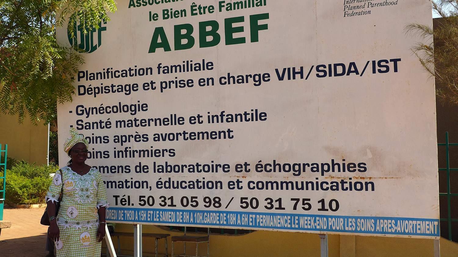 Adissa KONATE montre à l’entrée du siège de l’ABBEF les services que son organisation offre à la population. 