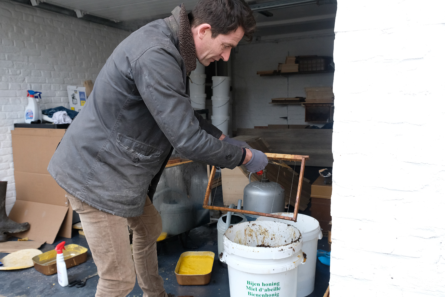Sylvain TOUSSAINT est en train de gratter la cire d’abeille présente sur les cadres de ses ruches.