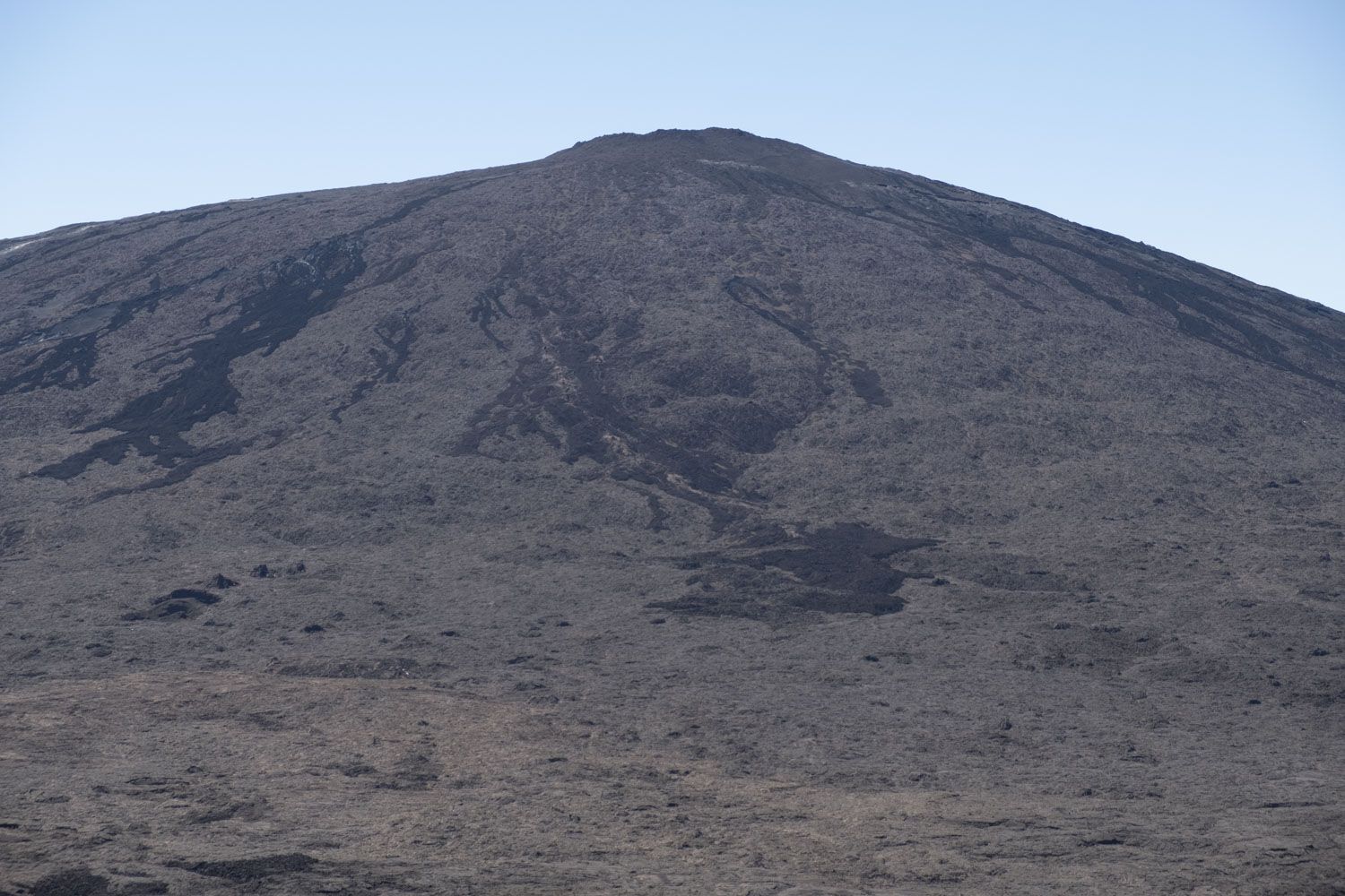 Vue du Pas de Bellecombe, le point de départ de la randonnée qui mène jusqu’au cratère du Piton de la Fournaise. Il faut environ 5 heures aller et retour pour admirer le cratère principal du volcan. Regardez bien sur le volcan, les traînées noires sont des anciennes coulées de lave. Elles sont refroidies, les randonneurs peuvent marcher dessus. 