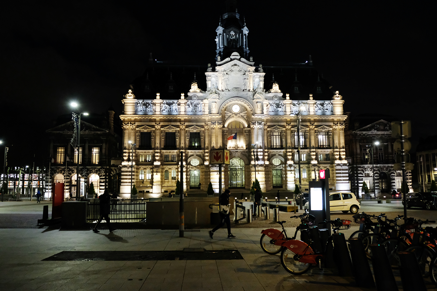 La nuit est tombée, l’occasion d’observer le bâtiment éclairé. La frise en dessous du toit représente les différentes étapes du travail de la laine : de la tonte du mouton au tissage dans les industries textiles qui ont fait la gloire de la ville. 