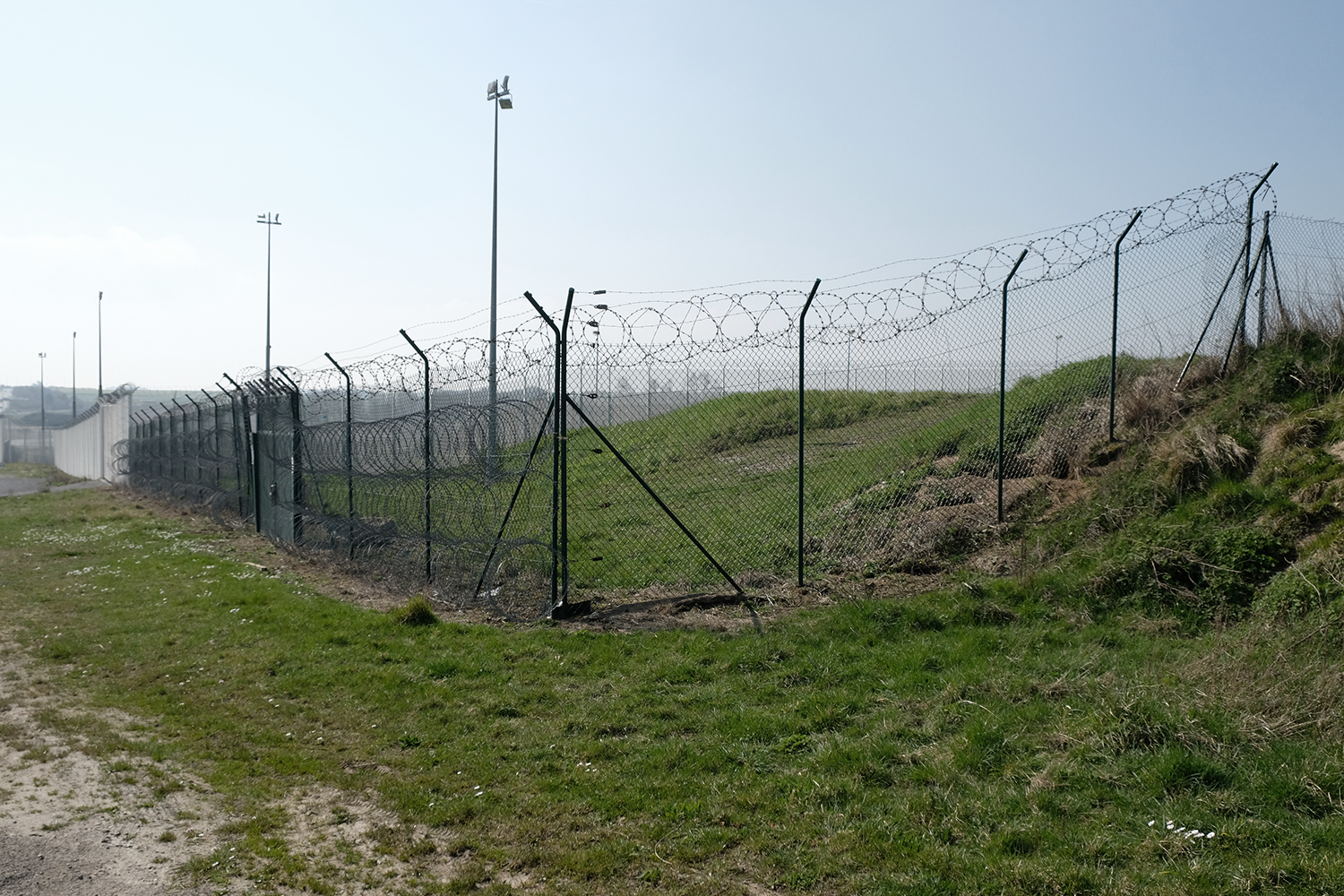 A quoi ressemble une frontière&nbsp;? Des grilles et des barbelés, encore. Nous sommes cette fois-ci ente Coquelle et Sangatte. Derrière les grillages, en contre-bas, l’entrée du tunnel sous la manche. 