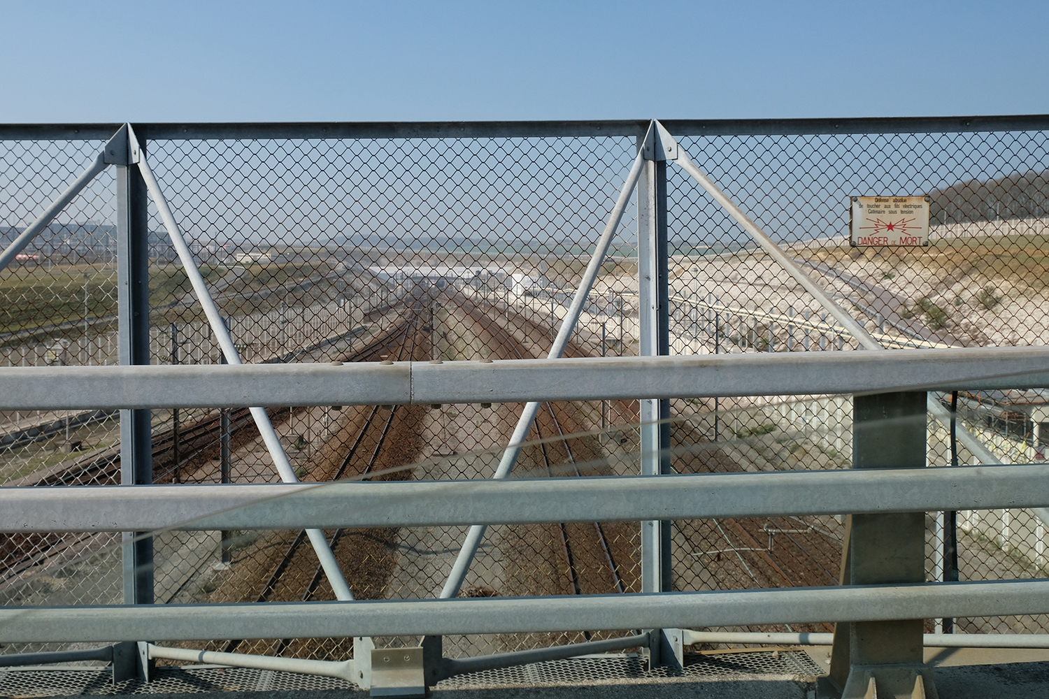A quoi ressemble une frontière&nbsp;? Quelques mètres plus loin, un pont nous amène au dessus des rails du tunnel sous la manche. En contre bas des voitures de police et des douanes surveillent le passage.