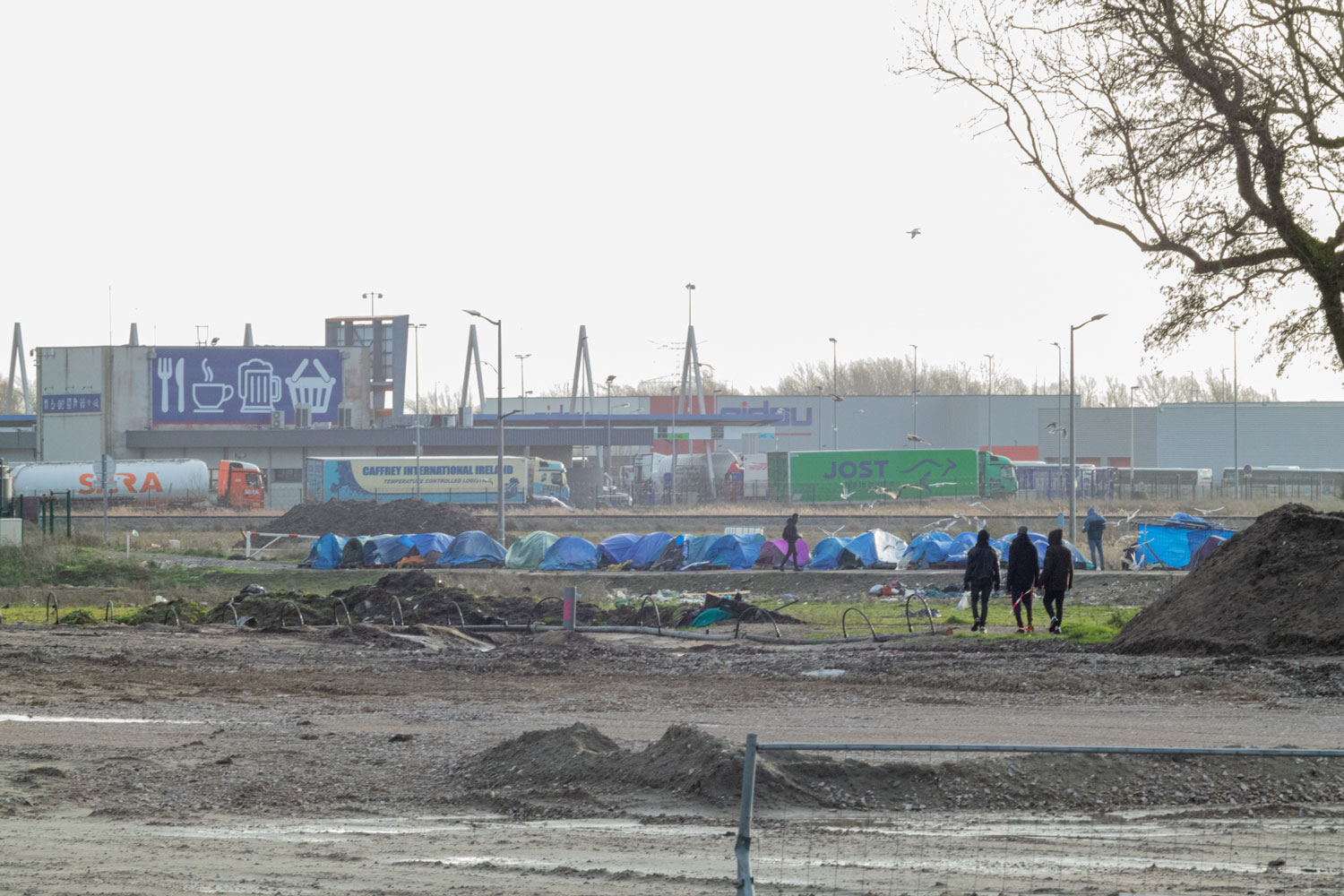 Un groupe de migrants rentre dans son camp de fortune, proche de l’autoroute.