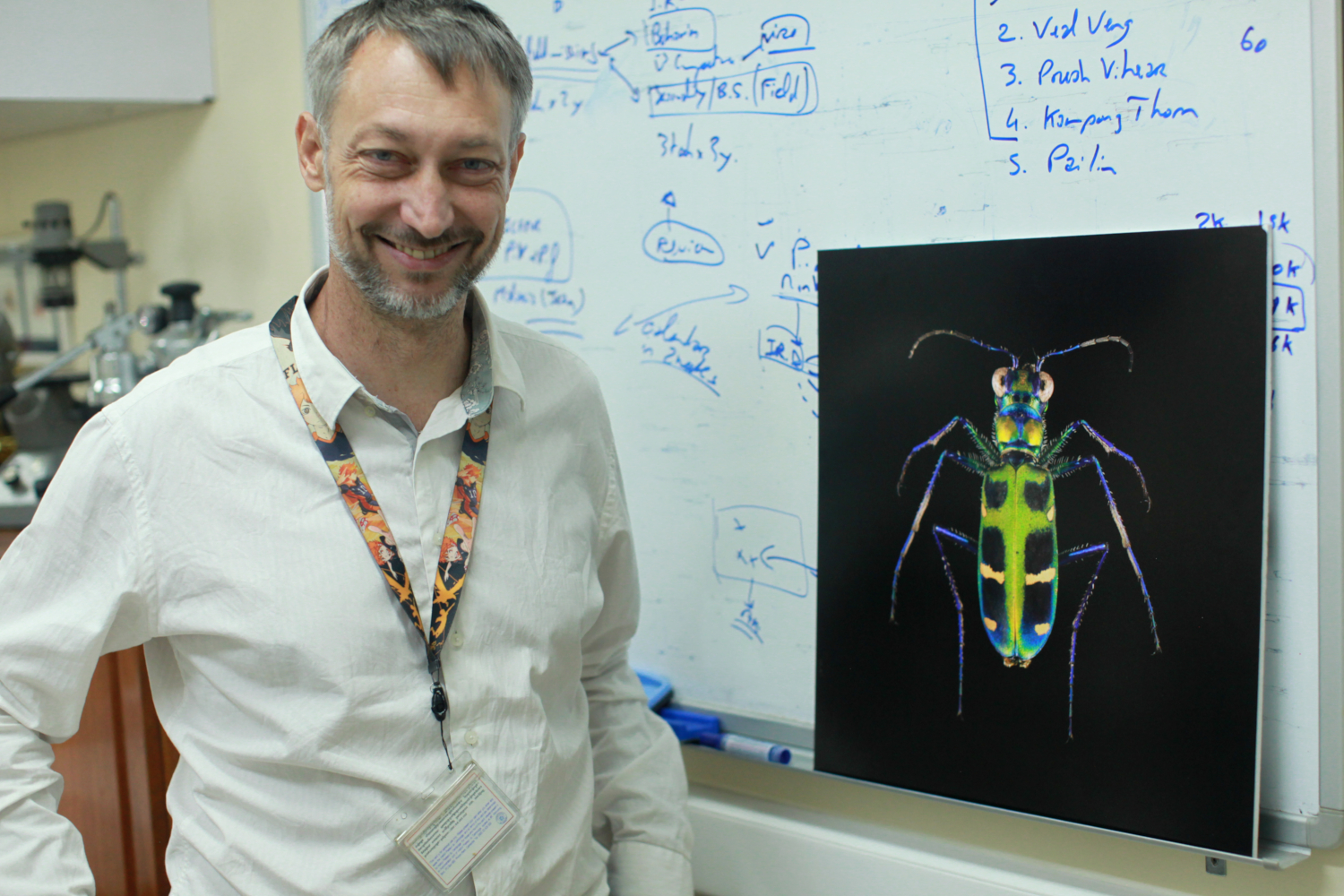Sébastien BOYER à côté d’une photo de l’exposition photographique sur les insectes organisée par l’Institut Pasteur de Phnom Penh à l’Institut français de Phnom Penh. Il s’agit d’une cicindèle (genre Cicindela) ©Globe Reporters